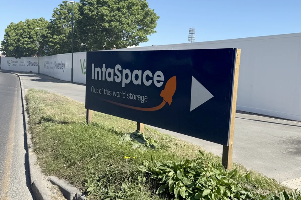 Blue outdoor signage in front of IntaSpace Self-Storage units in Croydon with the logo on.